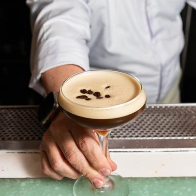 A bartender serves a glass of Espresso Martini on the counter.