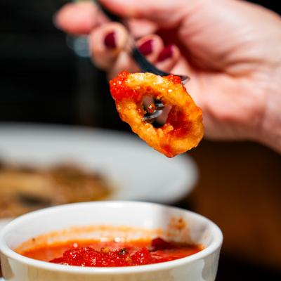 Hand holding a bite of calamari on a fork.