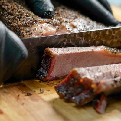 Hands in black gloves slicing smoked brisket.