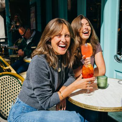 Three guests enjoy vibrant cocktails at table in the sunny outdoor setting.
