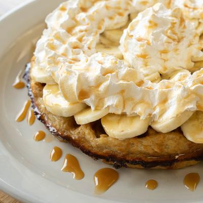Oatmeal waffle topped with banana slices, whipped cream, and a caramel drizzle.
