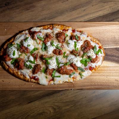 Meatball ricotta pizza with basil garnish, served on a wooden board.