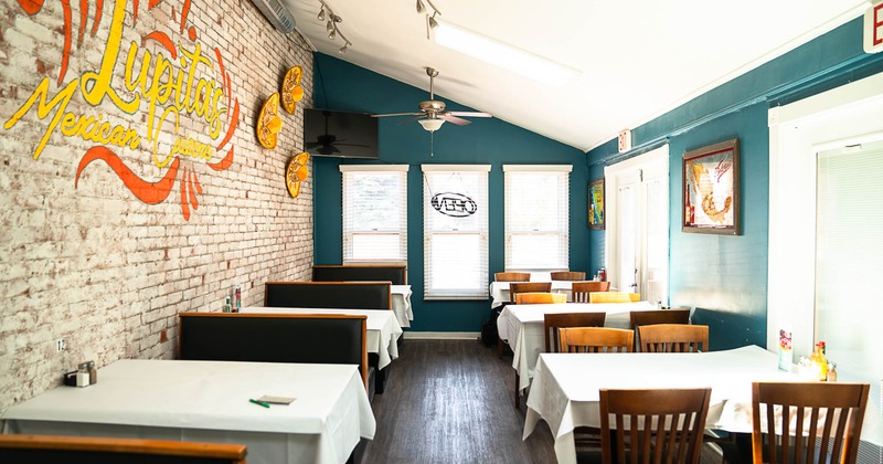 Dining room, tables with white tablecloths, chairs, and booths, restaurant trademark on a wall