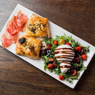 Burrata cheese on a bed of arugula, tomatoes, coppa, black olives and garlic bread.