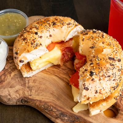 A halved bagel filled with cheese & tomato, accompanied by green sauce and sour cream..