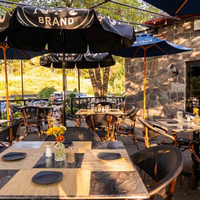 Outdoor seating with tables under large black umbrellas and stone wall in the background.