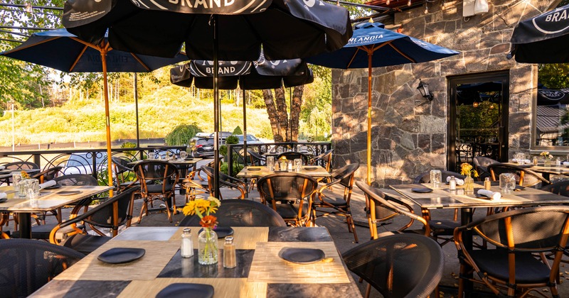 Outdoor seating with tables under large black umbrellas and stone wall in the background