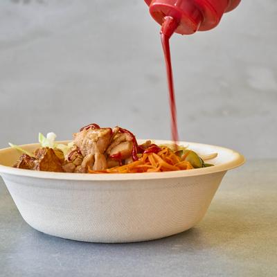 Pouring sauce over a chicken dish bowl.