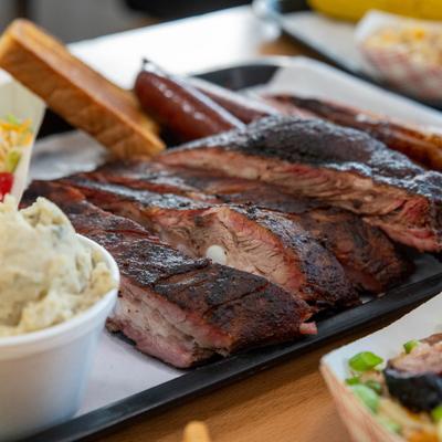 Close-up of grilled ribs with a crispy charred surface, accompanied with sides.