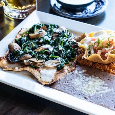 Spinach Chicken served with rice, beans, and a small taco salad in a tortilla bowl.