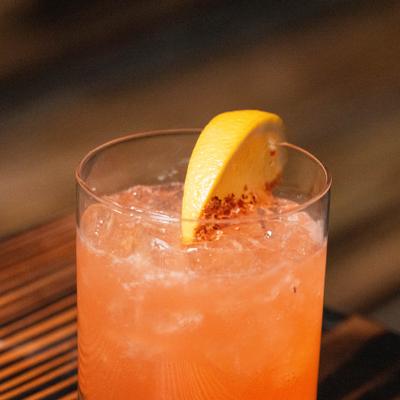 Iced orange cocktail in a rocks glass with lemon garnish and chili flakes.