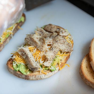 Avocado toast topped with shredded cheese and seasoned chicken.