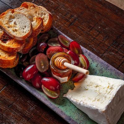 Burgundy board with grapes honey cheese and toasted bread.