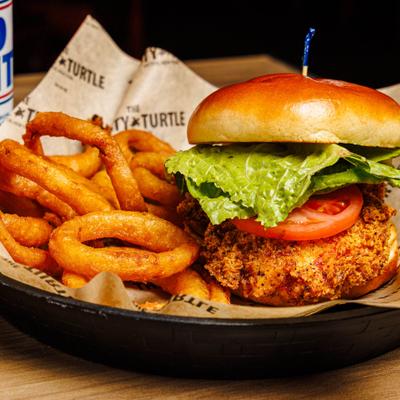 Chicken sandwich with lettuce and tomato, served with onion rings.