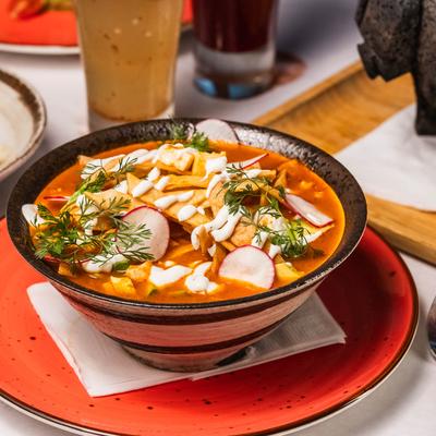 A bowl of soup with tortilla strings, chicken, and Oaxaca cheese.