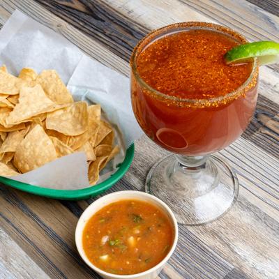 Michelada cocktail served alongside basket of chips and salsa.