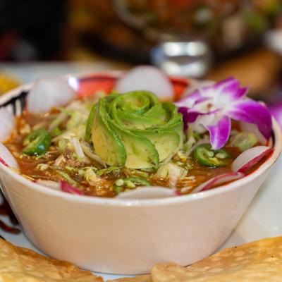 Mexican Pozole soup topped with avocado, radishes, and flowers.