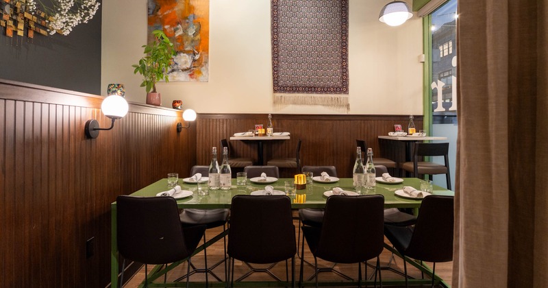 Dining area with a green table set with plates and glassware, surrounded by dark chairs