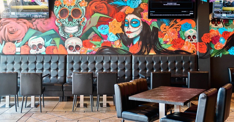 Vibrant Day of the Dead mural in a restaurant with skulls and calavera art above black leather seating and tables