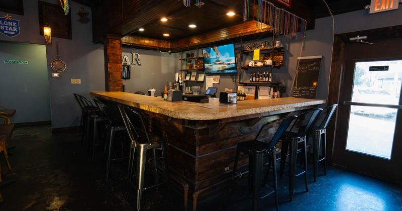 The interior of a bar with a wooden counter, metal stools, a flat-screen TV