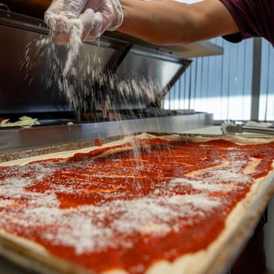 Pizza maker sprinkling grated cheese over a Sicilian style pizza.
