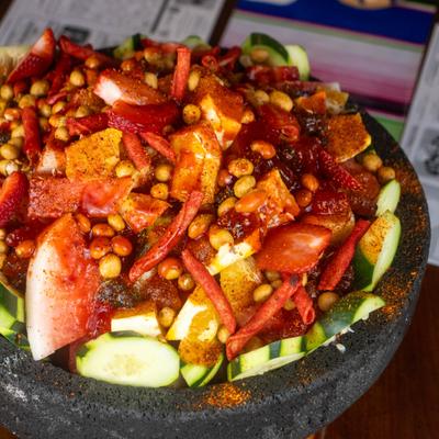 Fruit molcajete featuring cucumbers, peanuts, various fruits, and Takis chips.