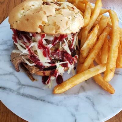 Beef sandwich with coleslaw and sauce, accompanied by crispy fries.