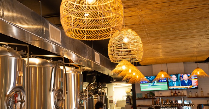 Industrial brewery interior with shiny metal tanks and woven rattan lights