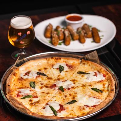 Margherita pizza served with a glass of beer and mozzarella sticks in the background.
