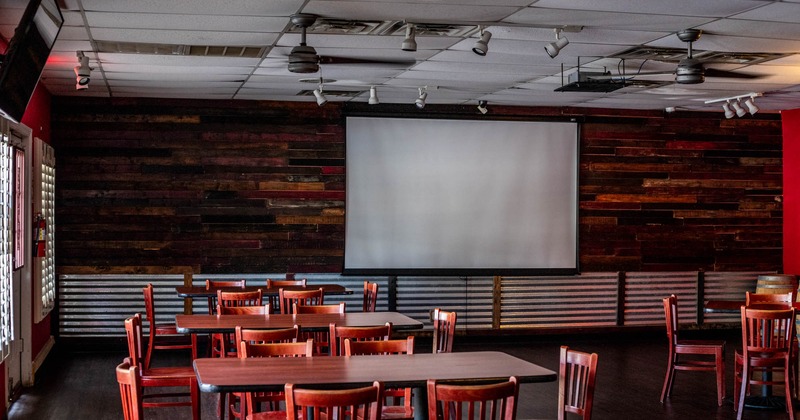 Room with tables, seats, and projection screen on the wall