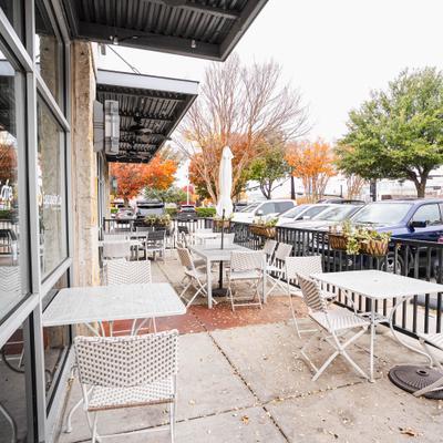 Sidewalk cafe patio featuring white metal tables and chairs.