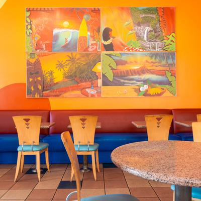Interior, tables and seating, colorful Hawaiian-themed murals on an orange wall.