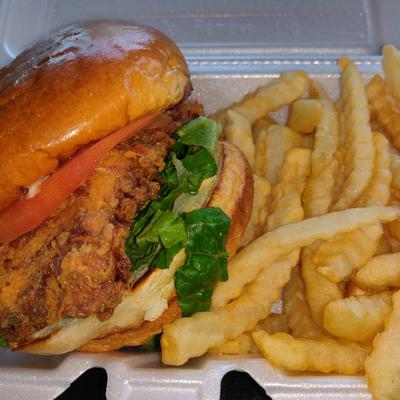 Fried chicken sandwich with lettuce and tomato in a shiny bun is paired with crinkle-cut fries.