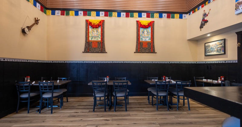 Interior of a culturally themed restaurant with wall hangings, prayer flags, and neatly arranged tables