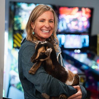 A guest is posing for a photo while holding a goat in their arms.