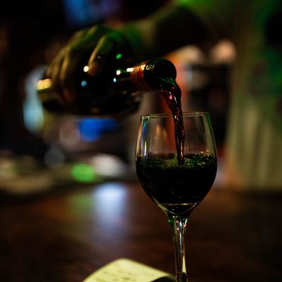 A person pouring red wine from a bottle into a crystal glass.