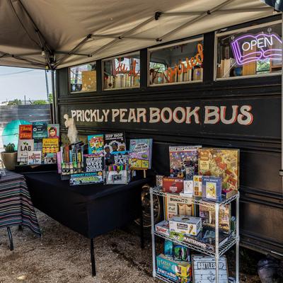 Outdoor book sale at Prickly Pear Book Bus, with colorful books and board games on display.