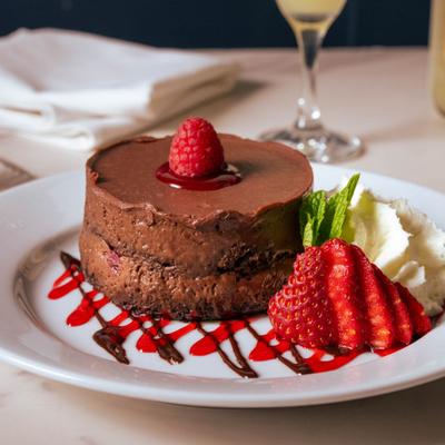 Chocolate mousse cake dessert garnished with whipped cream, raspberry, and strawberry slices.