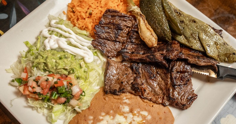 Grilled steak with rice, beans, guacamole, salsa, and peppers