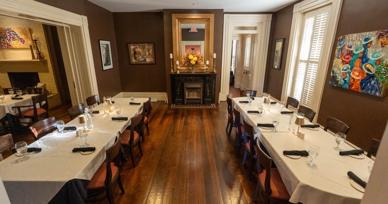 Elegant dining room with long tables, white tablecloths, wooden chairs, and a decorative fireplace