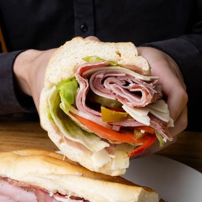 Hands holding a Italian sub sandwich featuring layers of cured meats, cheese and veggies.