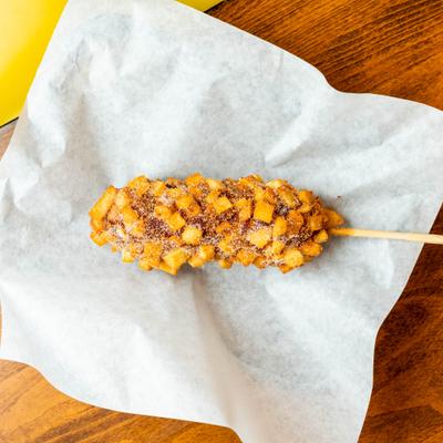 Potato-crusted Korean corn dog served on a stick.