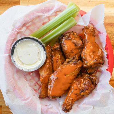 Chicken wings coated in sauce with celery sticks and dipping sauce on the side.
