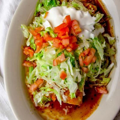 Burritos stuffed with beef, chicken, and beans, covered in red sauce, salad, and sour cream.