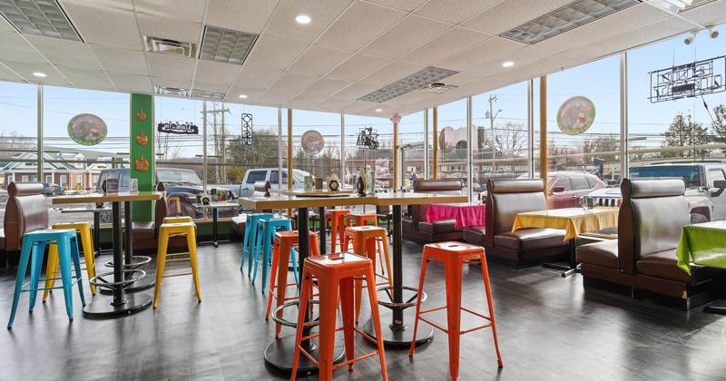 A brightly-lit dining area with colorful bar stools and booth seating near large windows.