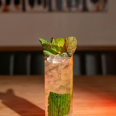 Tall glass filled with Mojito, crushed ice and mint leaves sits on a wooden table.