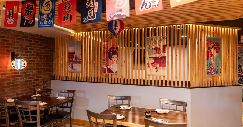 Interior, seating area, tables for four, thin wooden slats dividing wall, Japanese motif posters