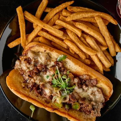 Steak and cheese sandwich with microgreens, served with fries.