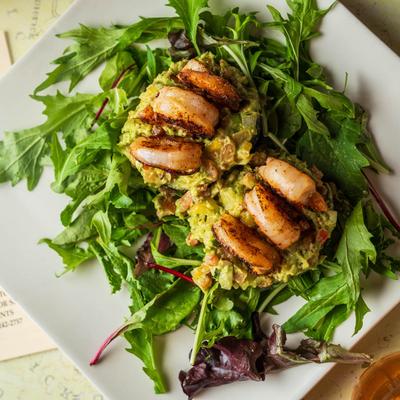 Mango shrimp atop avocado served over greens, top view.