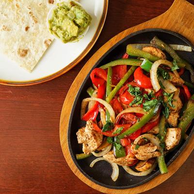 Chicken fajitas served with tortillas and guacamole.
